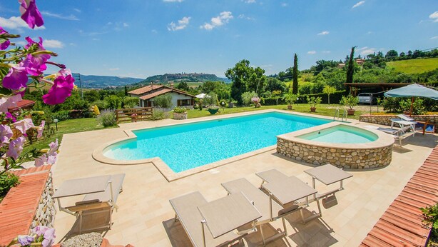 Ein Schwimmbecken mit Liegestühlen und einem Steinelement, umgeben von einem Garten und Blick auf Hügel.