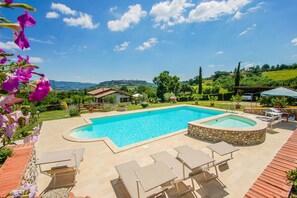 Una piscina con sillas de descanso y un elemento decorativo de piedra, rodeada de un jardín y vistas a las colinas.