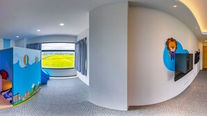 A modern hotel lobby with a curved wall, a large window with a view of a green field, and a children's play area with a colorful mural. - Plum Forest (Dongshan)