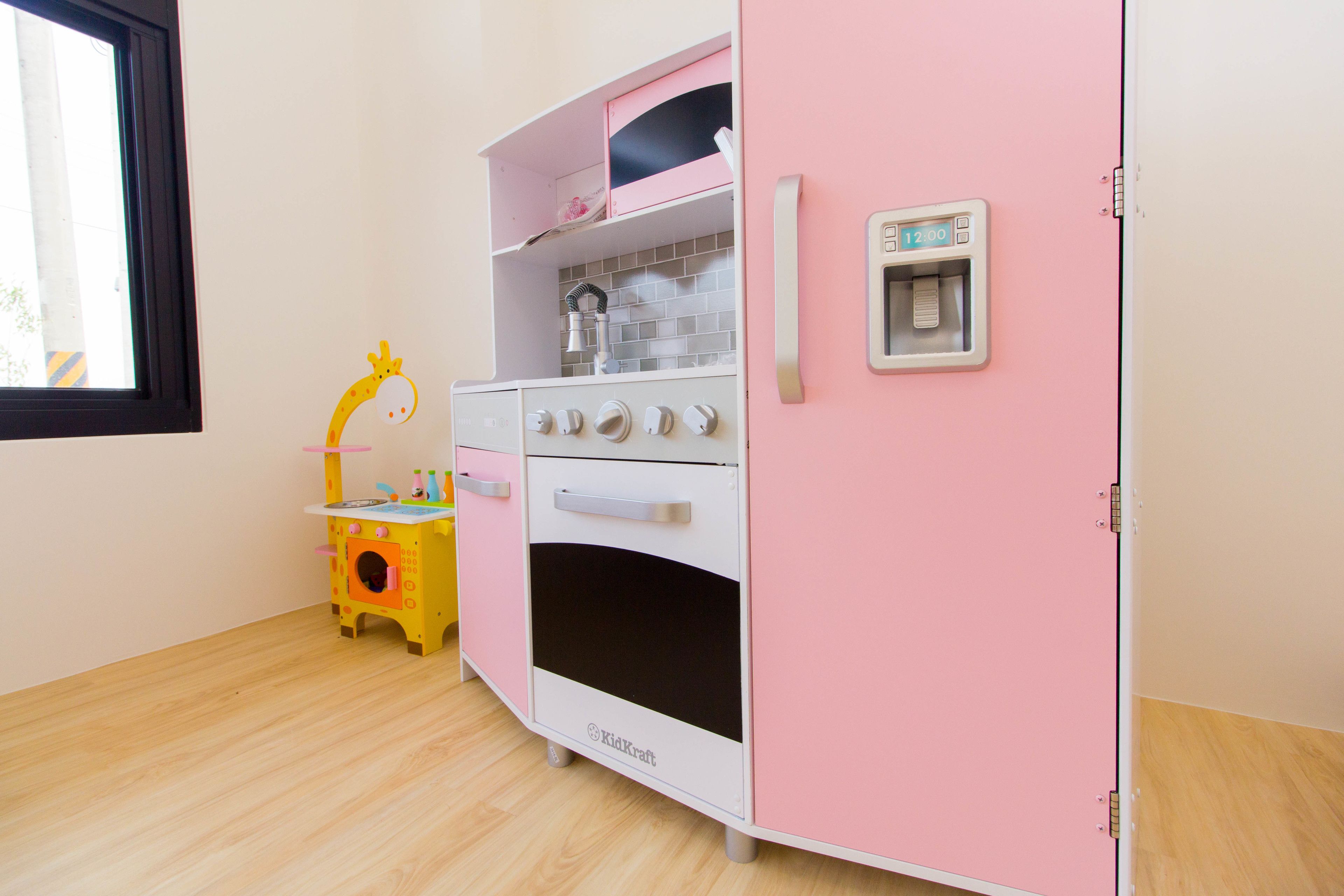 A children's play kitchen with a pink and white color scheme, featuring a sink, stove, and oven.