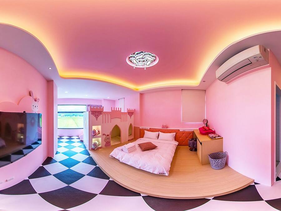 Un dormitorio con techo abovedado, una cama con almohadas, un televisor y una zona de juegos temática con castillo.