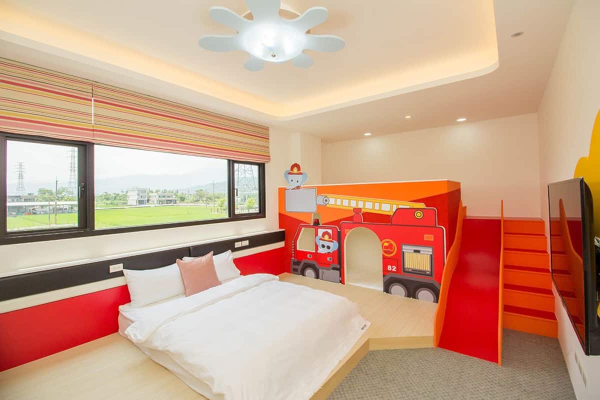 Ein kindgerechtes Zimmer mit Bett, einer Spielecke im Feuerwehrdesign und einem Fernseher.