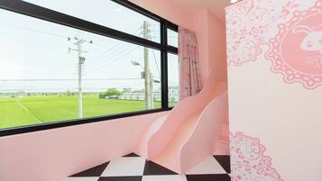 Una habitación con un ventanal grande, una pared rosa con motivos florales y un suelo a cuadros blanco y negro.