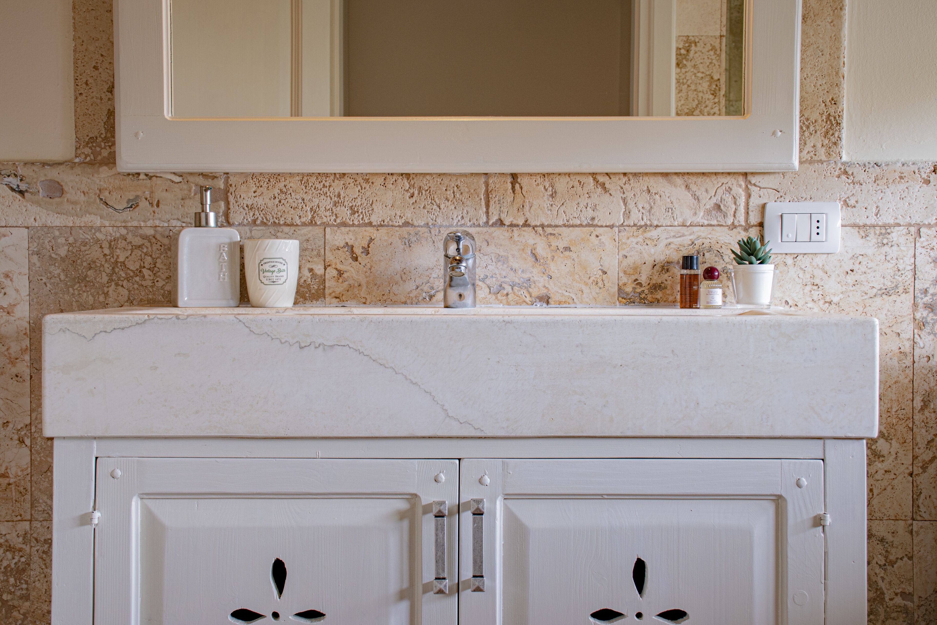 A bathroom with a marble countertop, a sink, a mirror, and a cabinet with two doors.