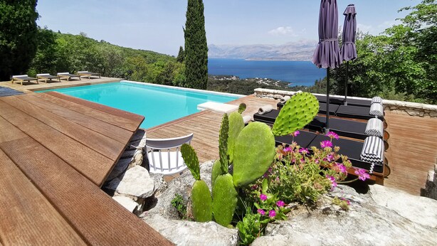 Ein Pool mit Holzterrasse, Liegestühlen und Meerblick.
