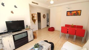 Ein Wohnzimmer mit Fernseher, einem weißen Sofa, einem roten Esstisch und einem Deckenventilator.