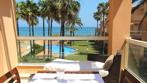 Ein Balkon mit Tisch für zwei Personen, Blick auf Pool und Palmen.