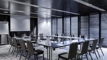 A conference room with a long table, chairs, a projector screen, and a large window with blinds.