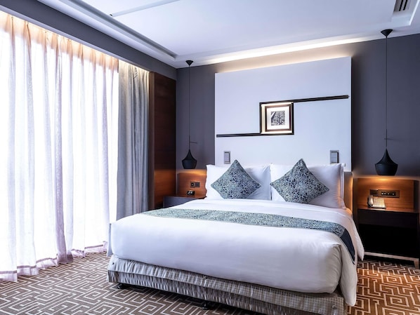 A modern hotel room with a large bed, a bedside table with a lamp, a wall-mounted artwork, and a patterned carpet. - Mövenpick Hotel & Convention Centre KLIA (Sepang)