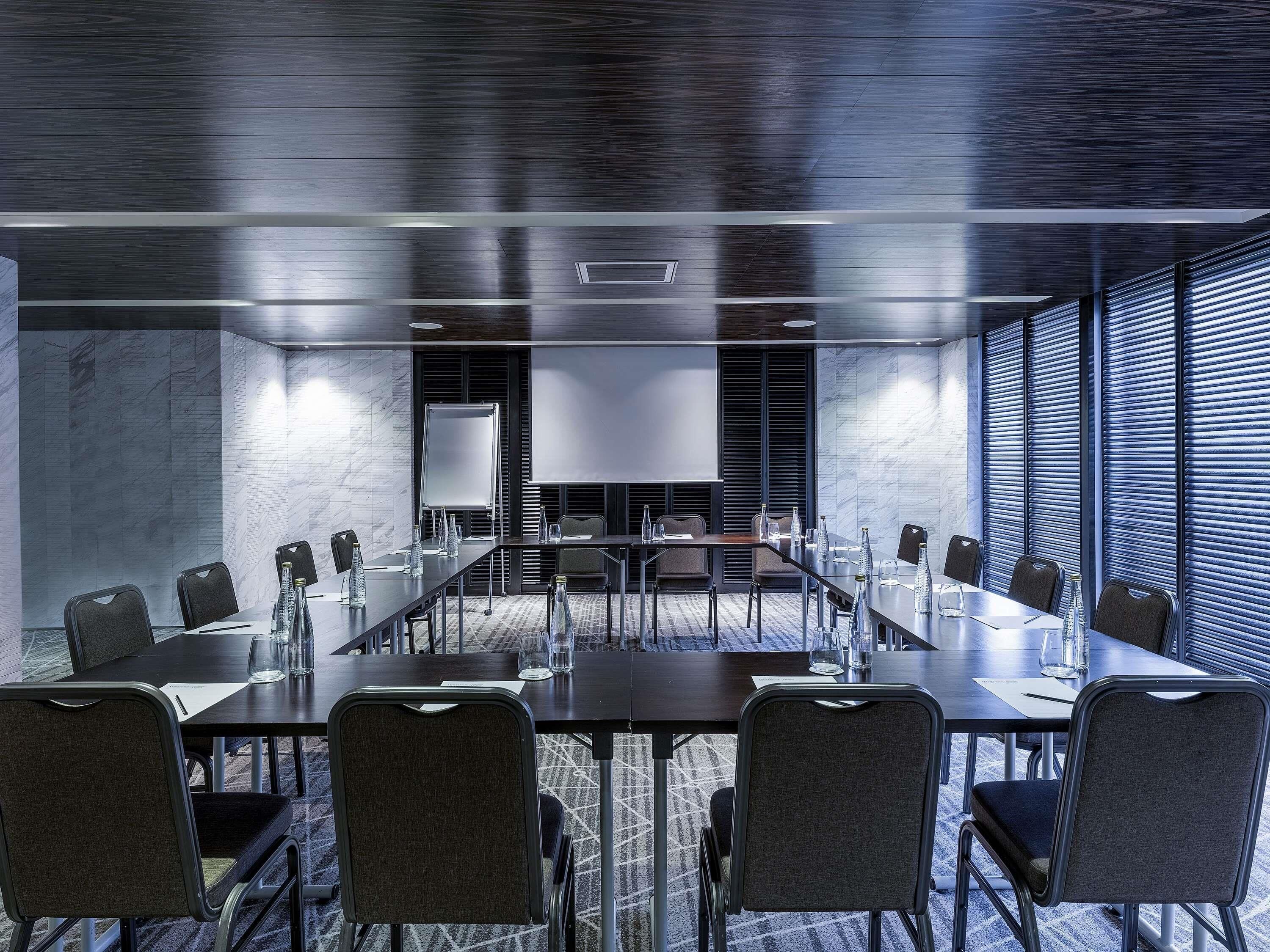 A conference room with a long table, chairs, a whiteboard, and a large window with blinds.