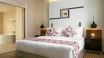 A hotel room with a large bed, a bedside table with a vase of flowers, a wall-mounted picture, and a bathroom with a bathtub and shower.