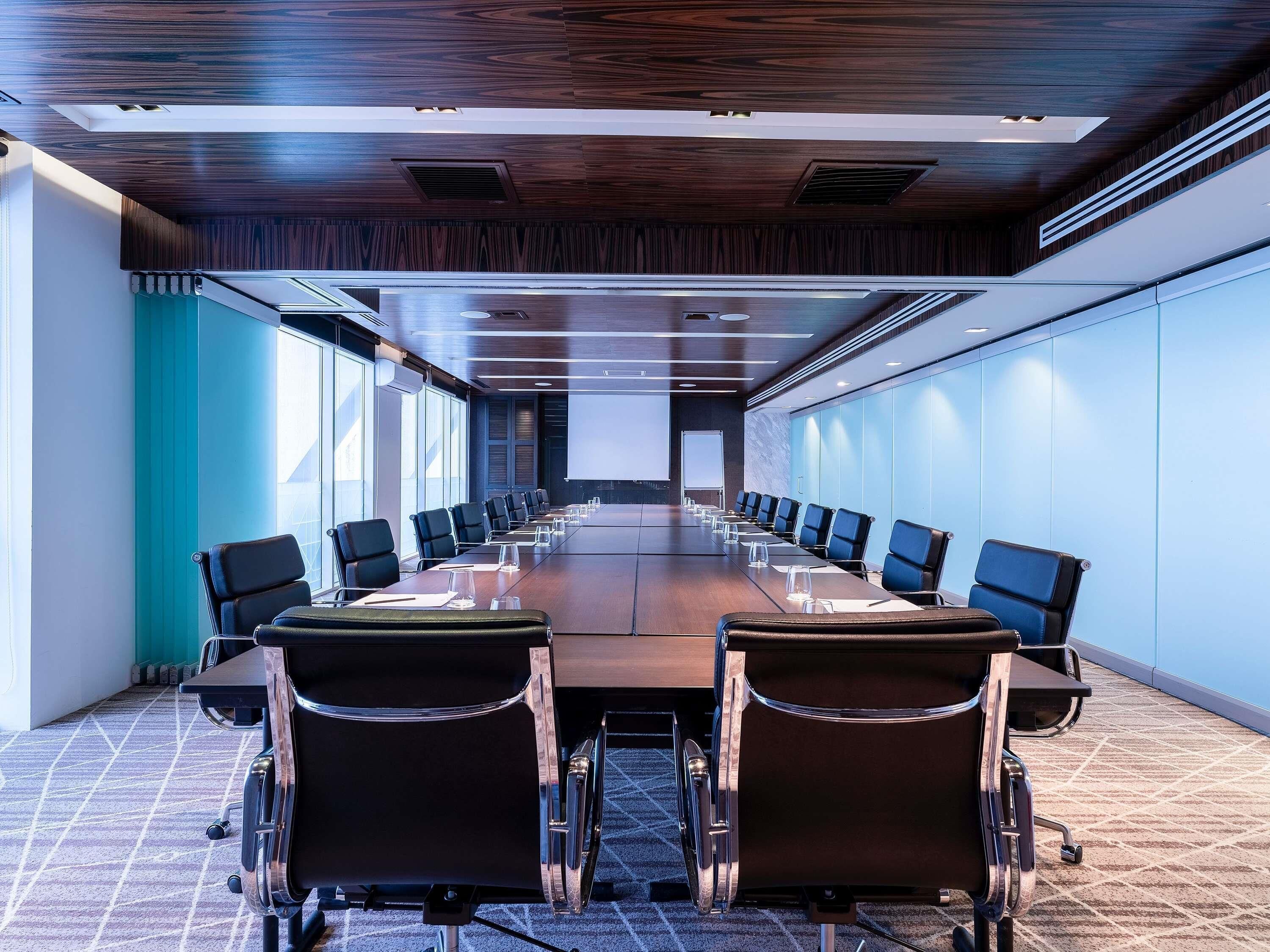 A conference room with a long table, chairs, and a projector screen.