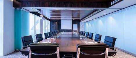 A conference room with a long table, chairs, and a projector screen.