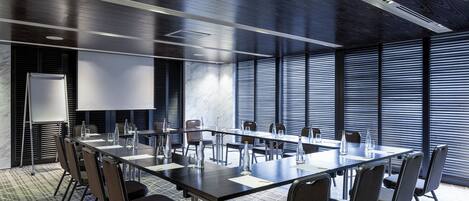 A conference room with a long table, chairs, a whiteboard, and large windows with blinds.