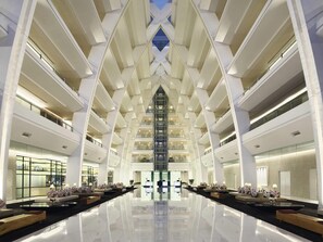 Un moderno vestíbulo de hotel con un atrio central, varios pisos y un suelo reflectante.