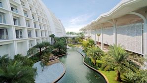A modern hotel with a central courtyard featuring a water channel, surrounded by lush greenery and palm trees. - Mövenpick Hotel & Convention Centre KLIA (Sepang)