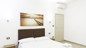 A neatly made bed with white linens, a wooden nightstand with drawers, a wall-mounted air conditioner, and a painting of a sunset over a pier. - IN FAIR 8: front fair, front fair elegant and comfortable residence (Bologna)