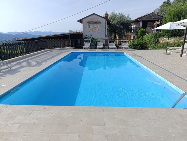 Une piscine rectangulaire, bordée d’une terrasse carrelée, entourée d’une clôture et agrémentée de quelques chaises longues.