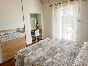 A bedroom with a bed, a desk, a chair, a mirror, and a window with curtains. - Bilocale Verde, relaxation in the countryside and exceptional views, private pool (Castelnuovo Magra)