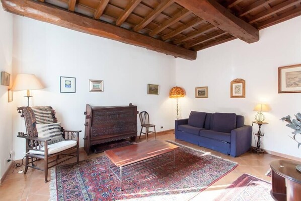A living room with a wooden ceiling, a blue sofa, a wooden coffee table, a patterned rug, and a wooden cabinet. - CHARMING APARTMENT CAMPO de'FIORI (Roma)