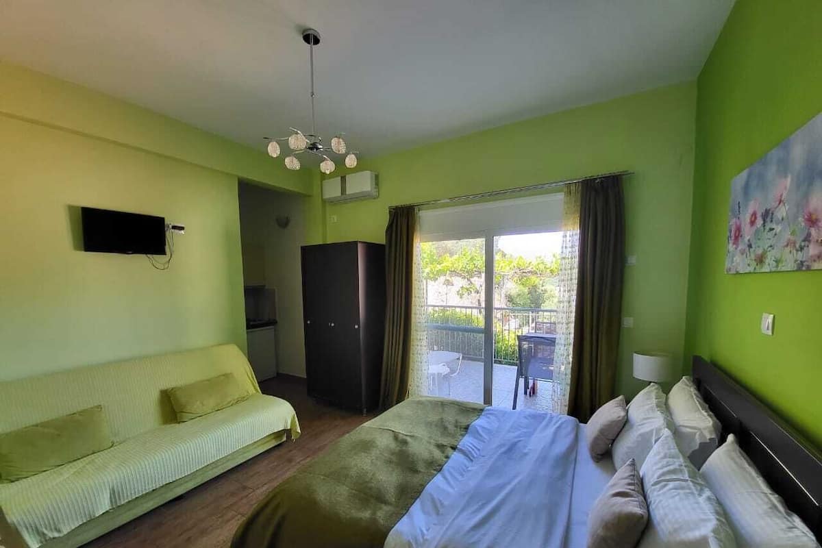 A hotel room with a bed, a sofa, a TV, and a balcony with a table and chairs.