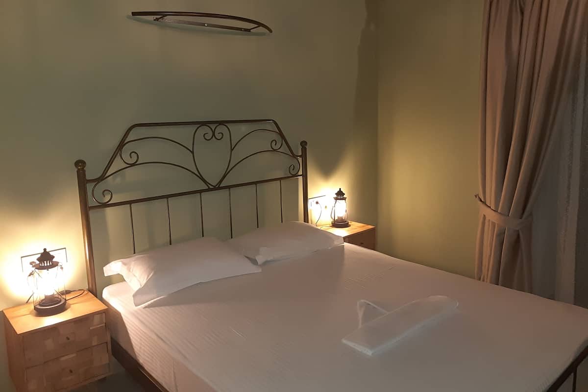 A neatly made bed with white linens, a decorative headboard, bedside lamps, and a wooden nightstand.