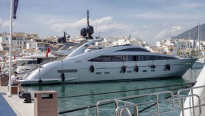 A large white yacht docked at a marina with a clear view of the surrounding buildings and a mountainous backdrop.