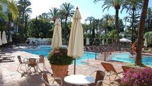 A poolside area with lounge chairs, umbrellas, and a swimming pool surrounded by palm trees.