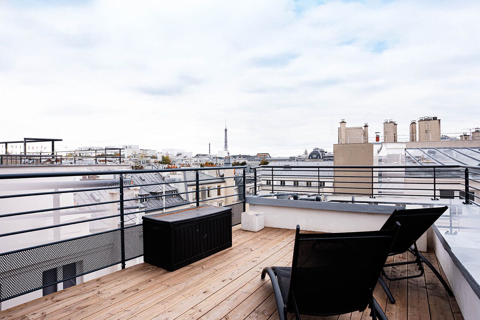Eine Dachterrasse mit Holzdeck, Metallgeländer und einem schwarzen Stuhl.