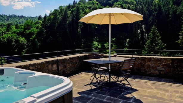 A hot tub and table with an umbrella on a stone patio with a forest view. - Medieval Tower Lungarno perfect location for inlove (Pratovecchio)