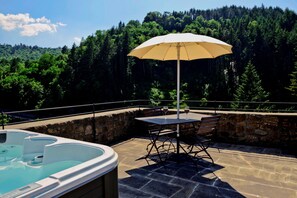 A hot tub and table with an umbrella on a stone patio with a forest view. - Medieval Tower Lungarno perfect location for inlove (Pratovecchio)