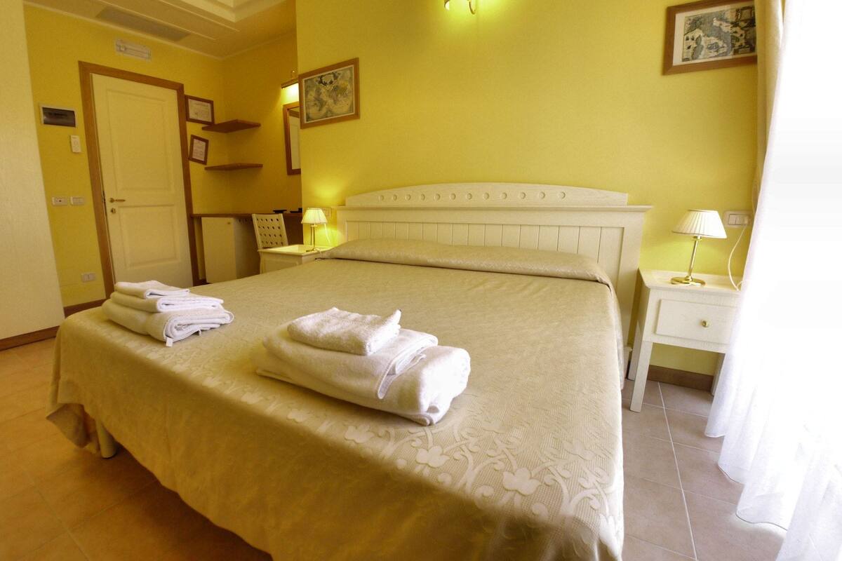 Una habitación de hotel con cama, mesita de noche, silla, escritorio y armario.
