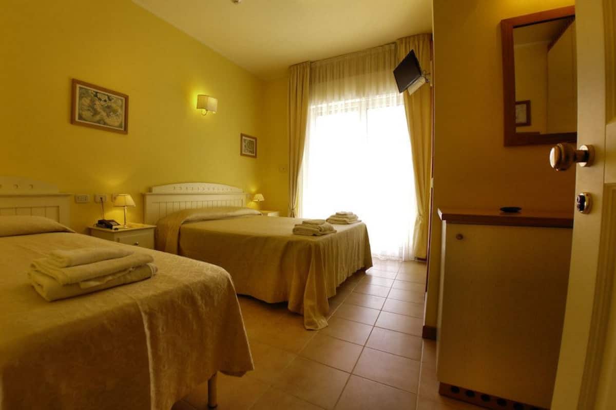 Habitación de hotel con dos camas, una mesita, una lámpara de noche, un televisor y una puerta.
