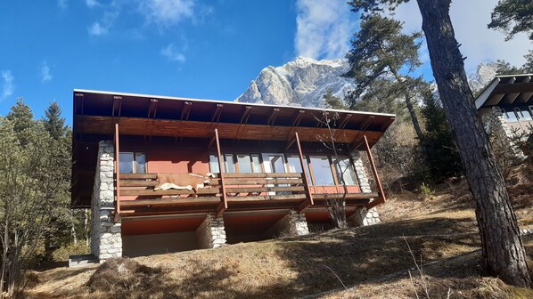 Une cabane dotée d’une terrasse en bois, de fondations en pierre et offrant une vue sur les montagnes.