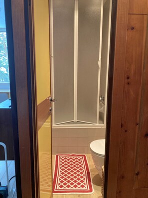 Une salle de bain avec une douche, des toilettes et un tapis rouge et blanc à motifs sur le sol.