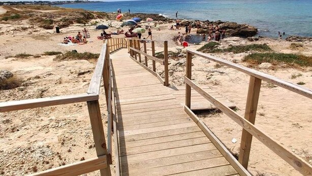 A wooden boardwalk leading to a beach with people sunbathing and swimming.
