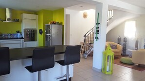 A modern kitchen with white cabinets and a green accent wall, a dining area with black chairs, and a living room with a sofa and a green lantern. - Villa 8 people, swimming pool. Open view. Beaches 15 mins away, quiet. (Roquefort-Les-Pins)