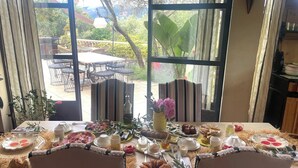 A dining table set with various dishes and drinks, large windows with a view of outdoor furniture and greenery. - Mas de Provence en Riviera (La Roquette-sur-Var)