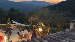 An outdoor seating area with wicker chairs and a table, surrounded by greenery and a view of distant mountains. - Mas de Provence en Riviera (La Roquette-sur-Var)