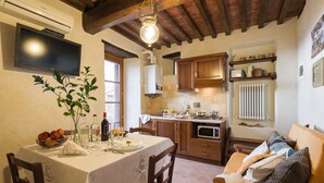 A cozy kitchen with a dining table set for two, a sofa, and a TV mounted on the wall. - Romantic shelter for 2, amazing view and large equipped terrace (Cortona)