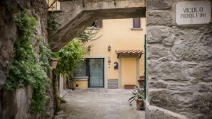 A narrow alleyway with a stone wall on one side and a building entrance with a door and window. - Romantic shelter for 2, amazing view and large equipped terrace (Cortona)