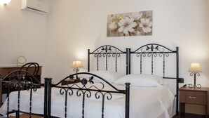 Un dormitorio con una cama doble, dos mesitas de noche con lámparas, un aire acondicionado de pared y un cuadro con motivos florales.