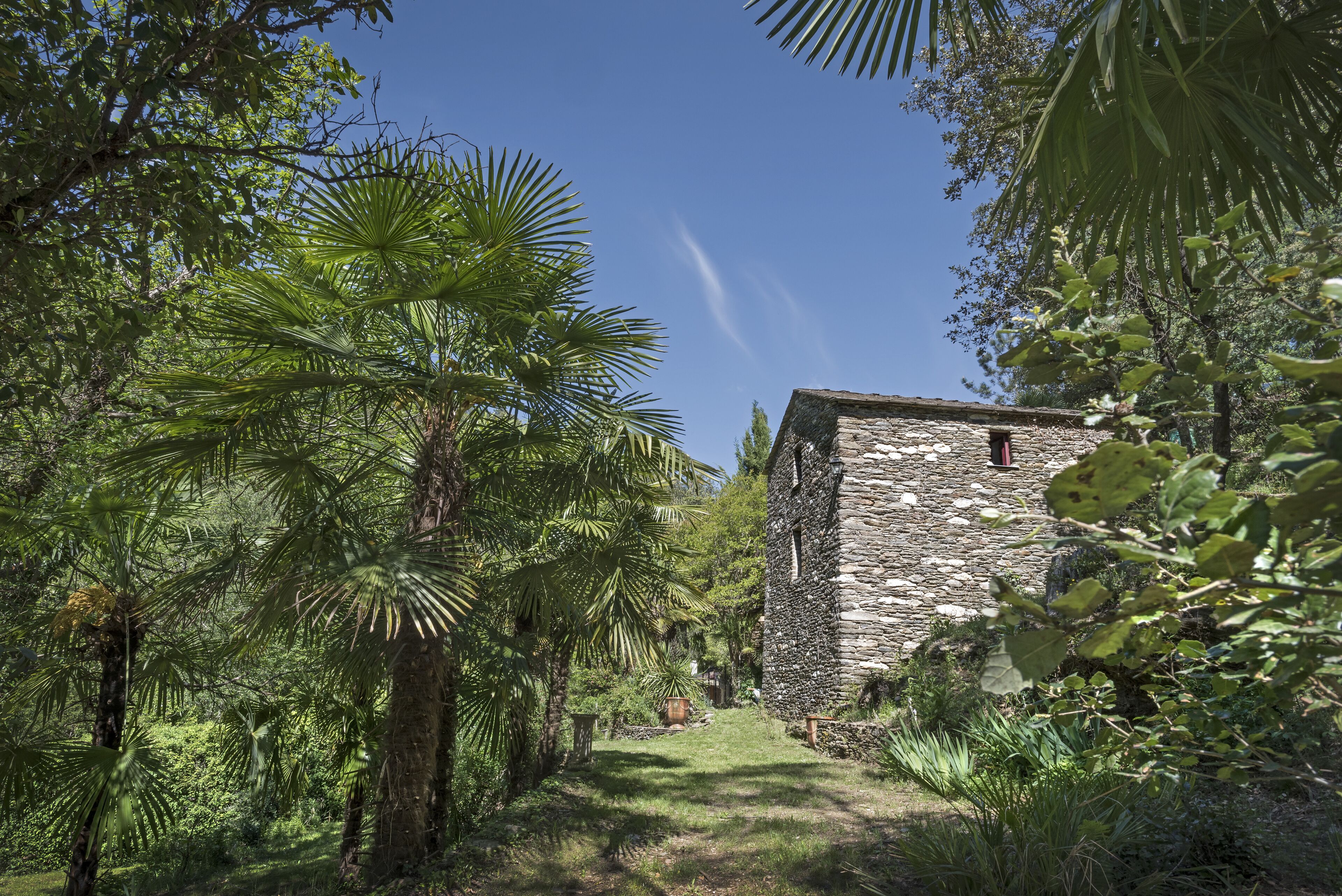A stone building surrounded by lush greenery and a clear blue sky.