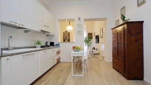 Une cuisine moderne avec des meubles blancs, un coin repas avec une table et des chaises blanches, et un meuble en bois sur la droite.
