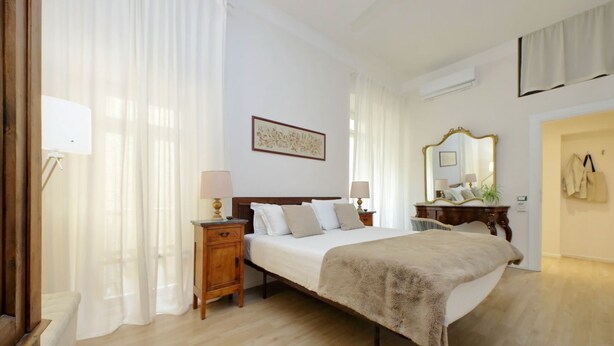 Une chambre à coucher avec un lit, des tables de chevet, un miroir et une fenêtre avec des rideaux.