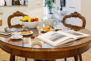 Een eettafel met een fruitschaal, een theepot, een croissant, een kopje en een open tijdschrift.