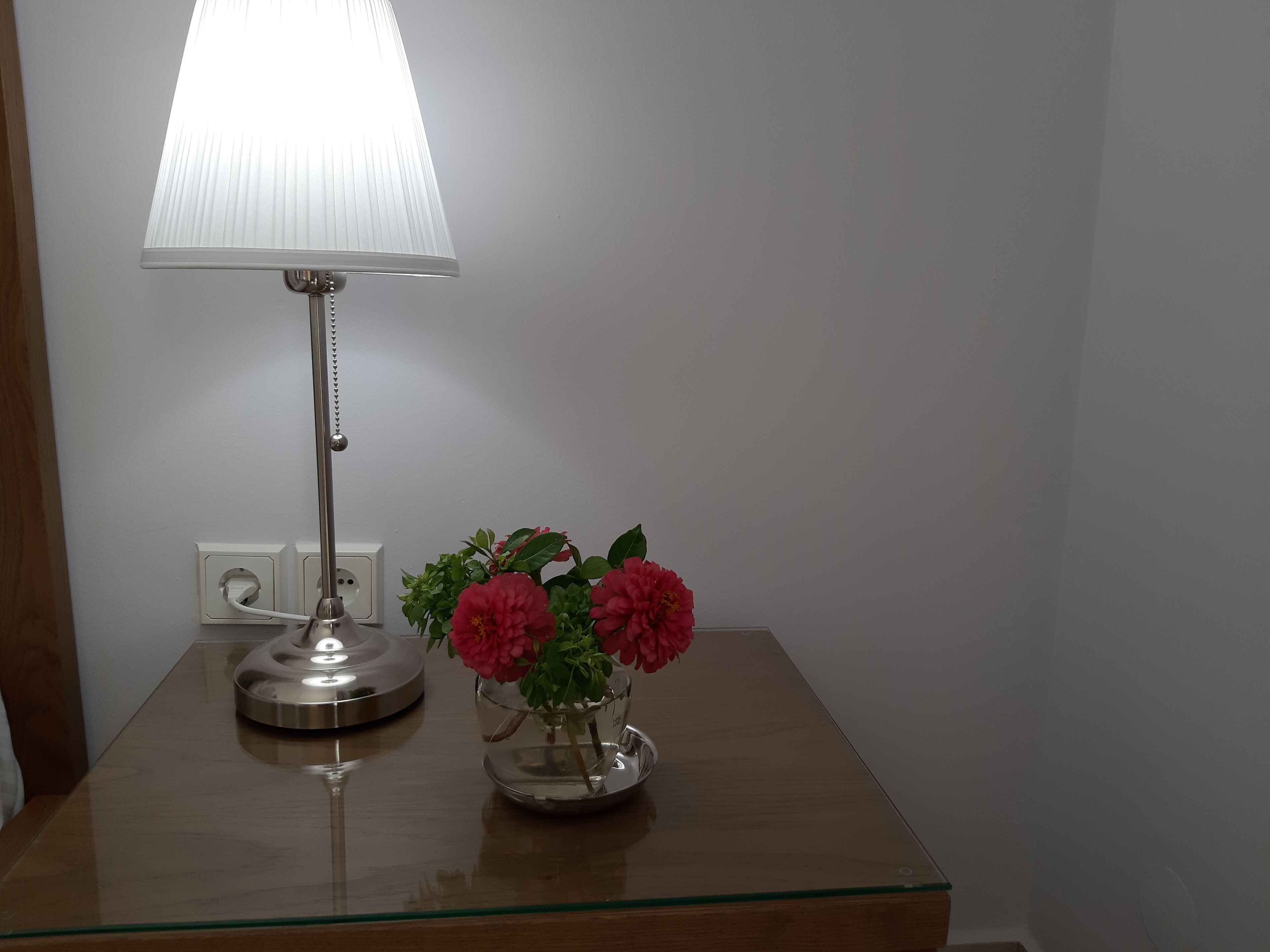 A bedside table with a lamp and a vase of flowers.