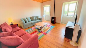 Una sala de estar con techo de madera, un sofá gris, un sofá rosa, una mesa de centro, un televisor y una chimenea.