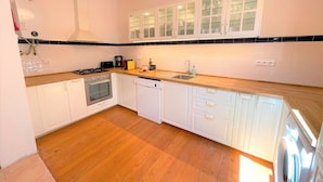 Una cocina con armarios blancos, encimera de madera, estufa, lavavajillas y pileta.
