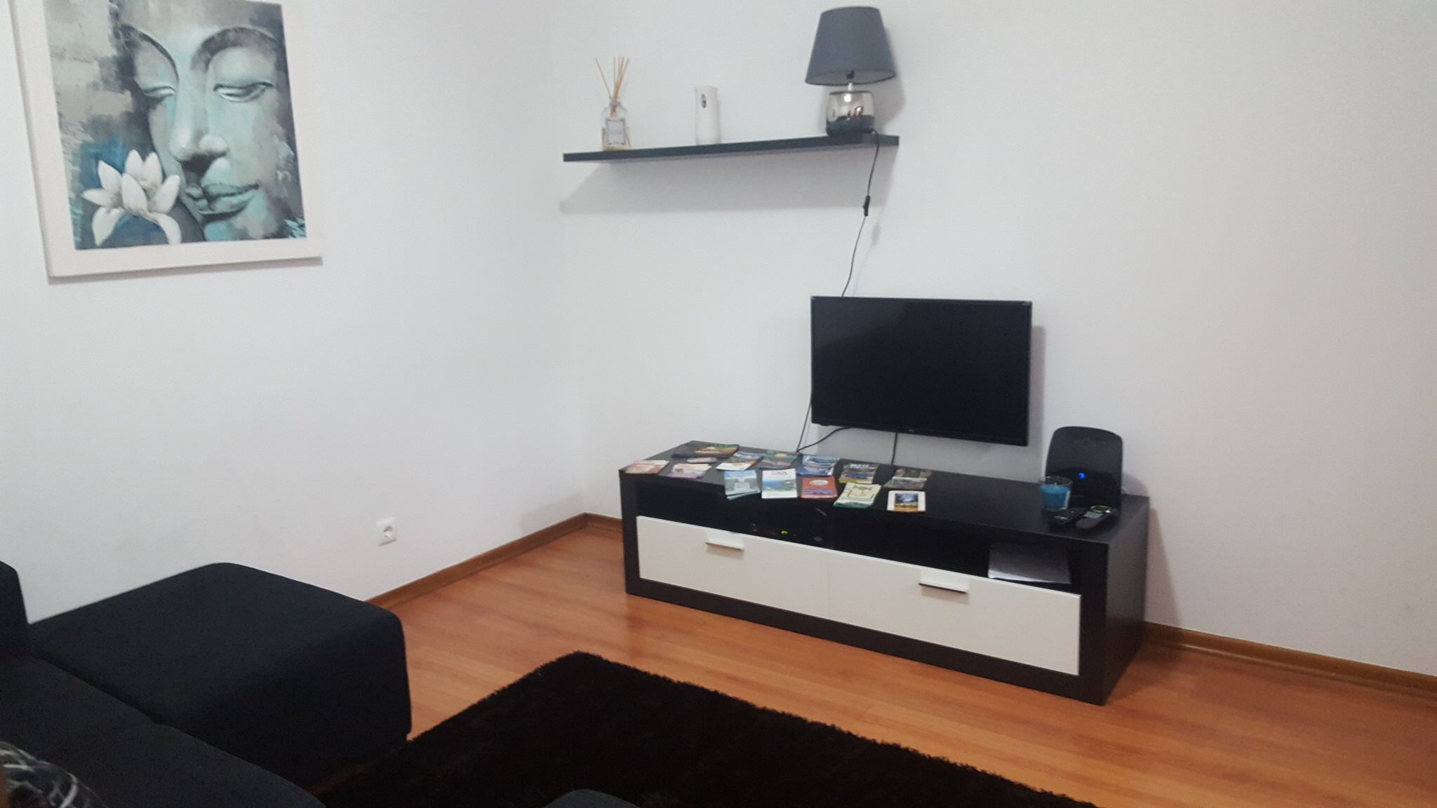 A modern living room with a black entertainment unit, a flat-screen TV, and a small shelf with decorative items.